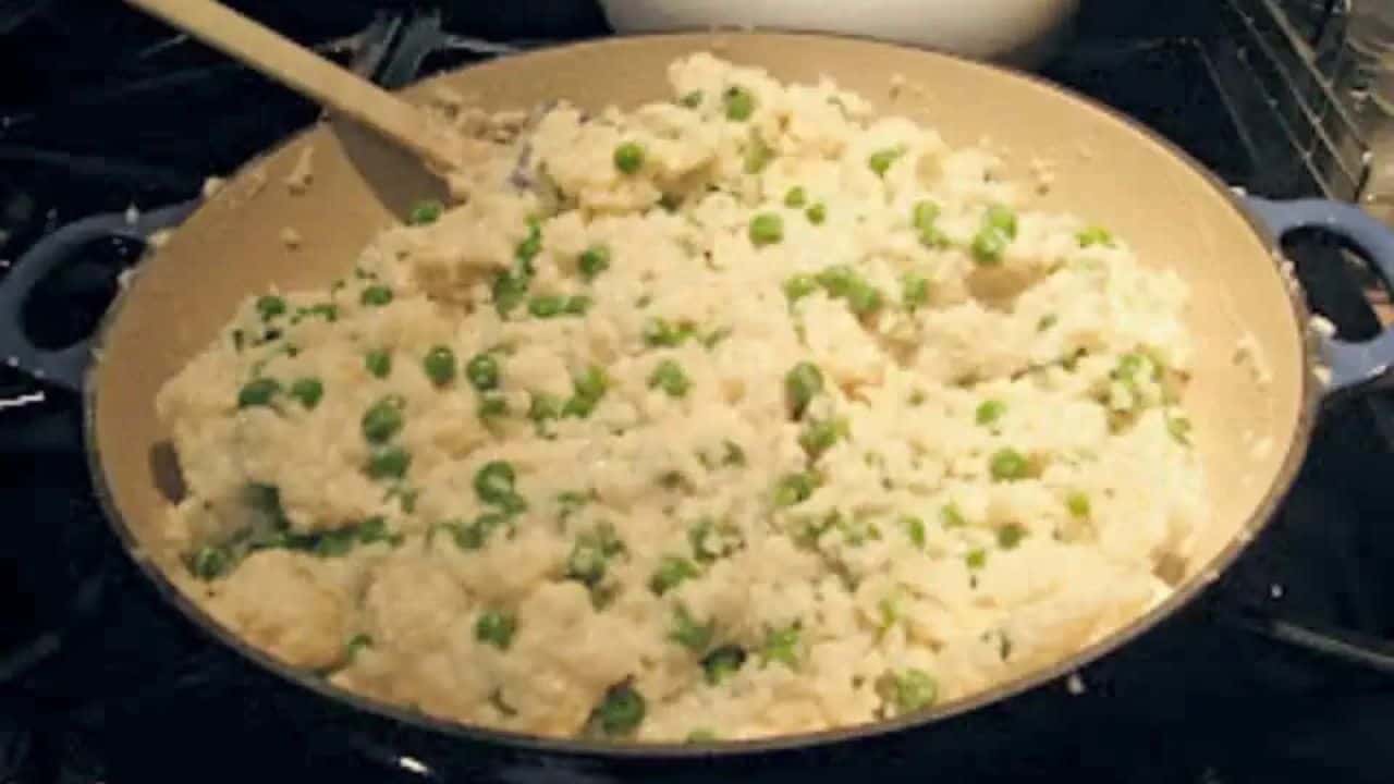 Image shows Chicken and pea risotto on a spoon with more in a green bowl behind it.