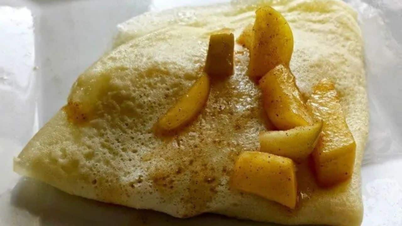 Image shows a close up of Cinnamon Apple Crepes with apples on top of a crepe folded into quarters.