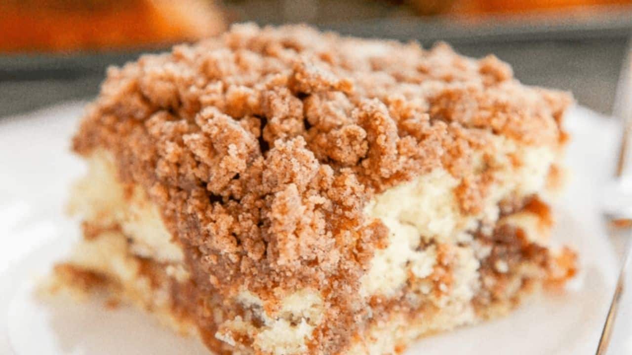 A slice of crumb-topped coffee cake with layers of cinnamon sugar crumble and moist yellow cake on a white plate.