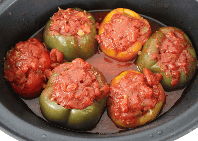 Six stuffed bell peppers, filled with a tomato-based mixture, are arranged in a large black cooking pot with visible sauce.
