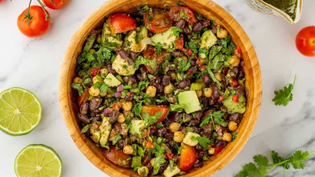 An overview of a bowl of dense bean salad surrounded by fresh ingredients.
