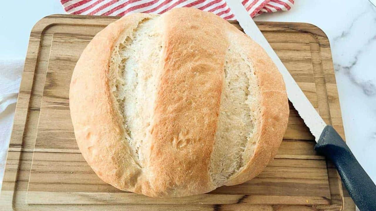 A loaf of peasant bread on a cutting baord with a knife with it.