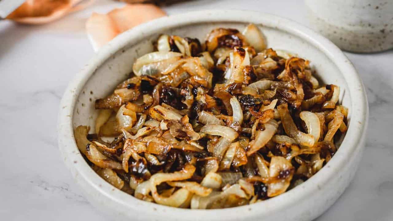 A ceramic bowl filled with cooked, browned caramelized onions sits on a white surface.
