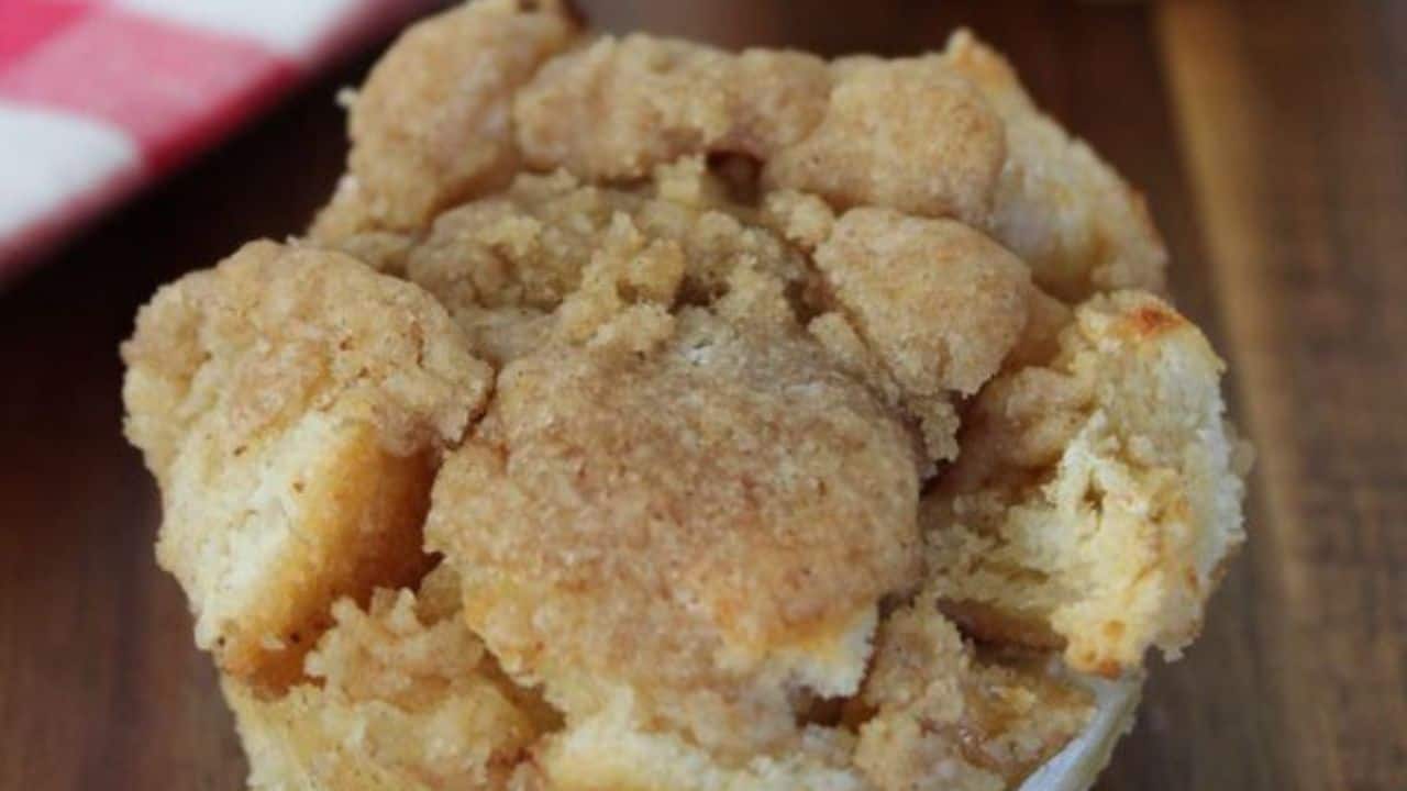 A close-up of a muffin topped with a crumbly cinnamon streusel on a wooden surface.