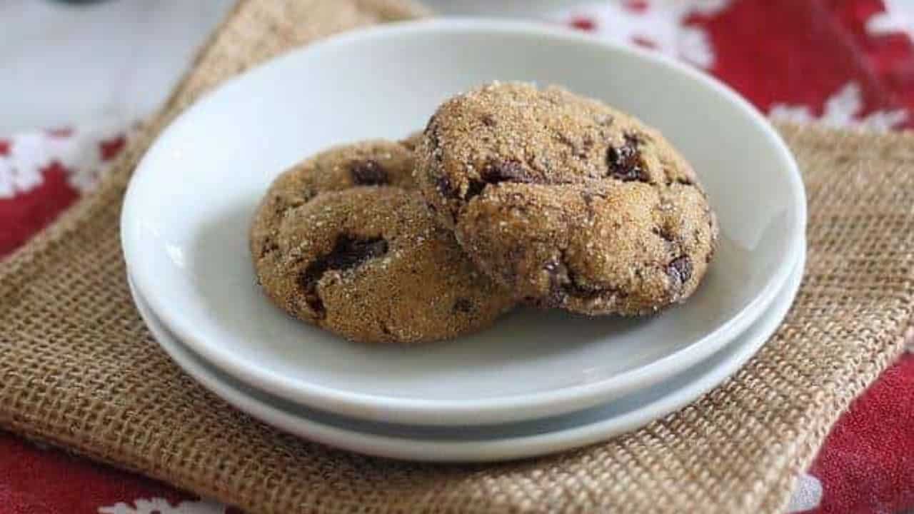 Three gingerbread molasses chocolate chunk cookies stacked on a white plate coated in sugar.