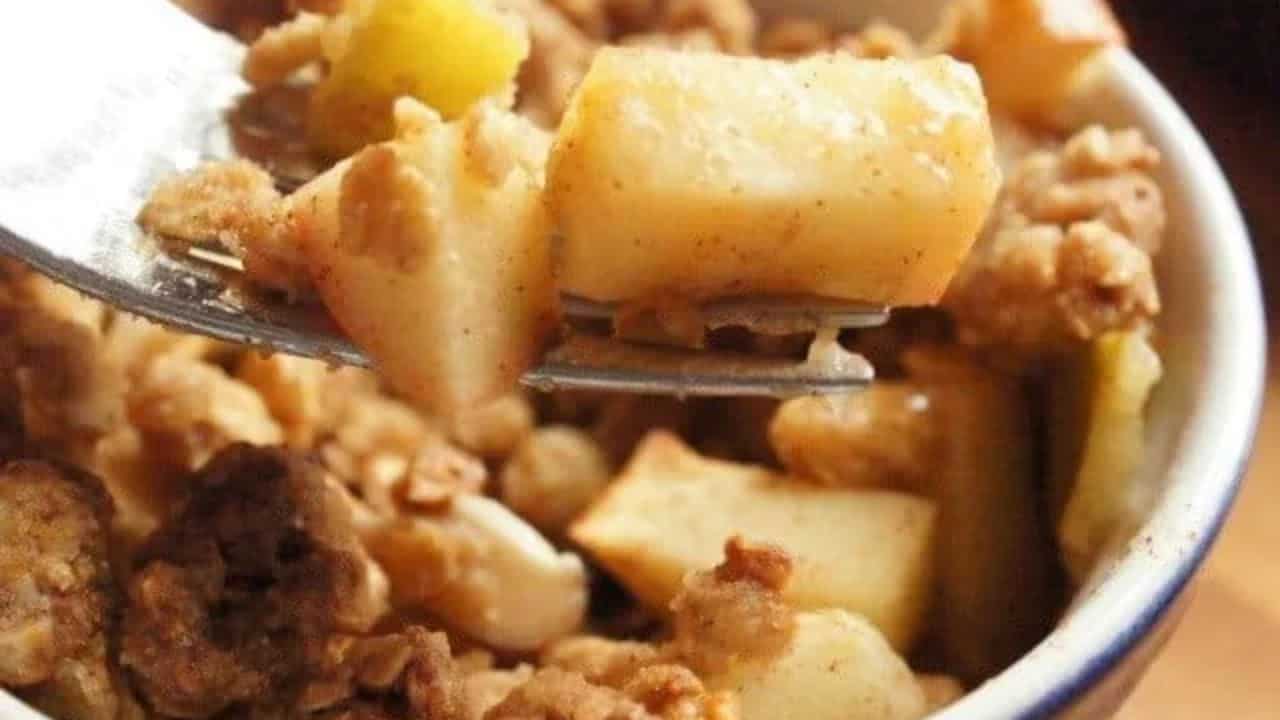 Image shows a close up of a fork holding a bite of Granola Apple Crisp with the whole serving behind it.