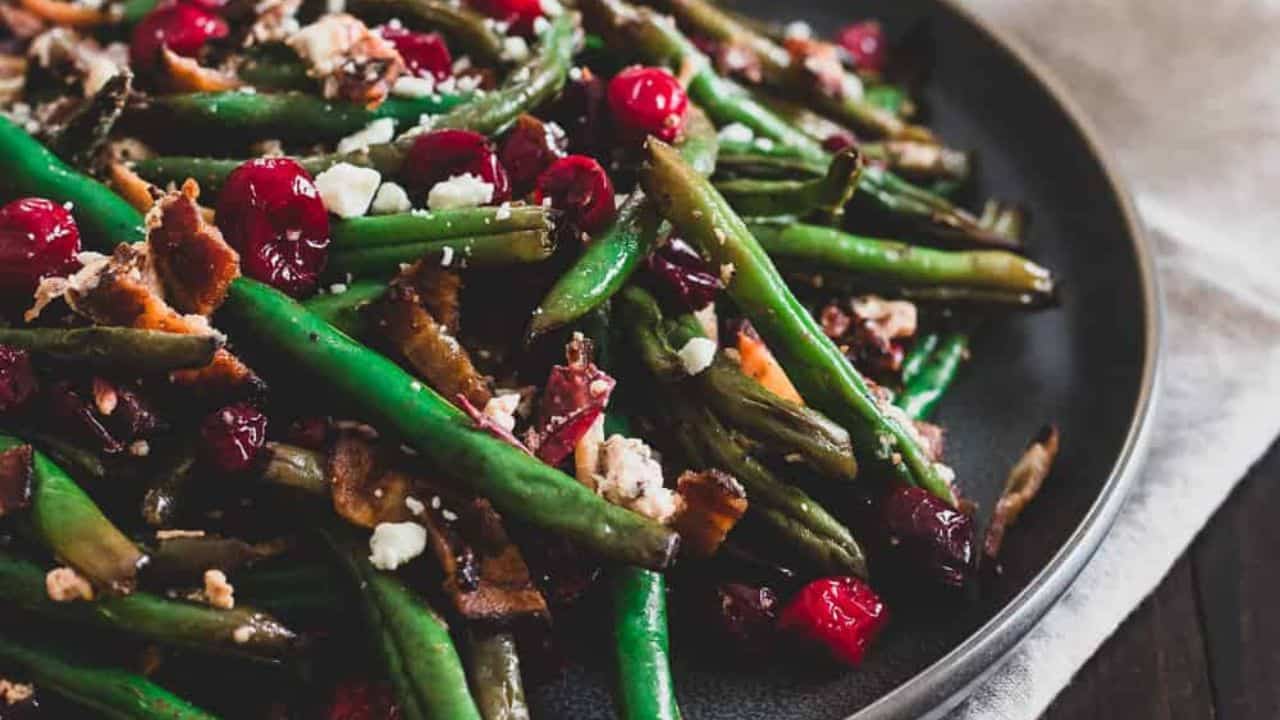 Green beans and cranberries on a plate with bacon and goat cheese.