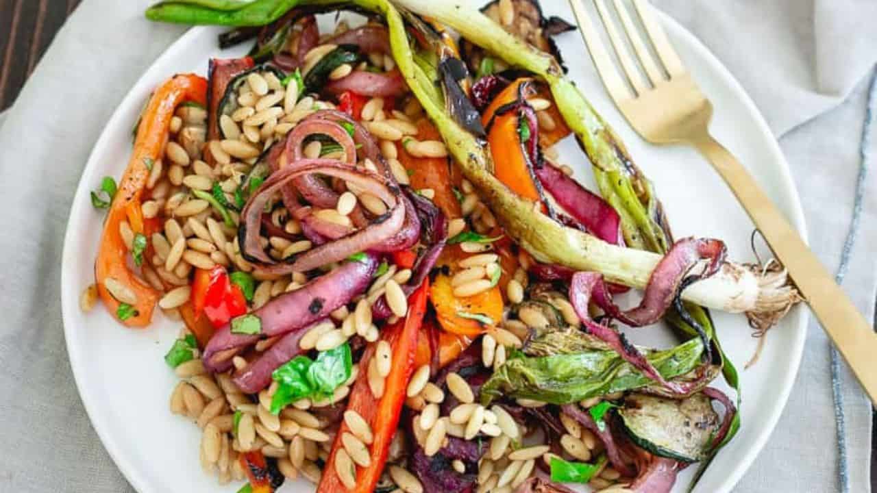 Grilled summer vegetables with orzo on a white plate with a fork.