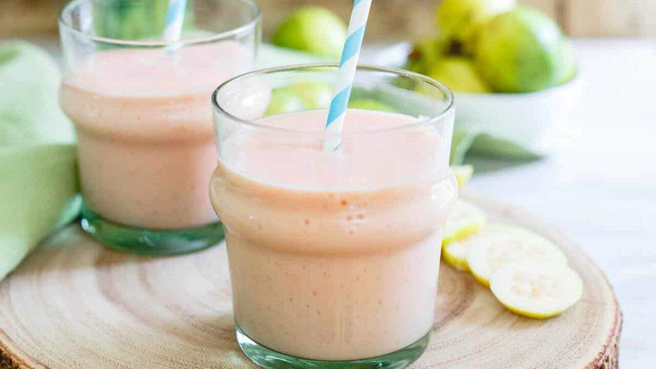 Guava pineapple smoothie in glasses with blue striped straw.