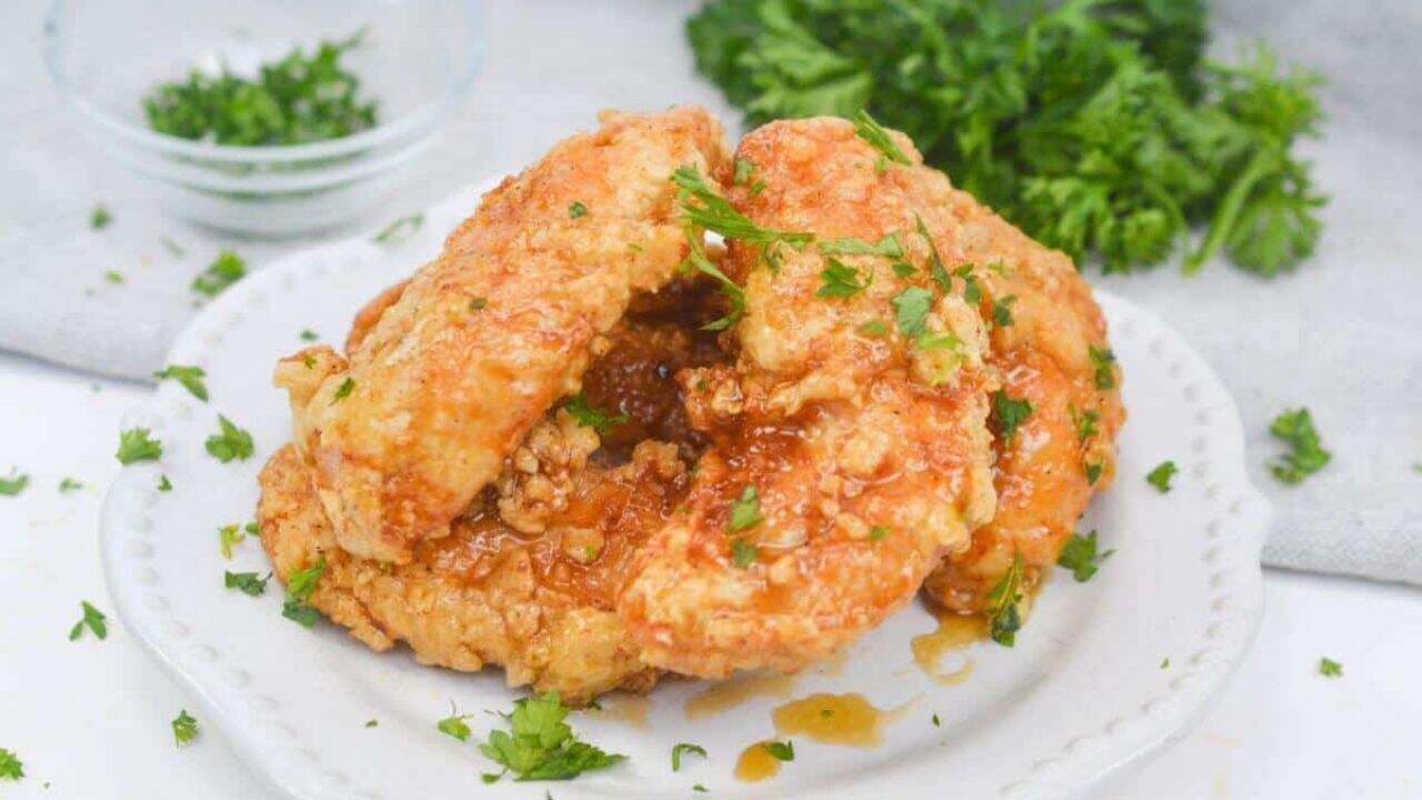 Serving of honey butter chicken garnished with parsley on plate.
