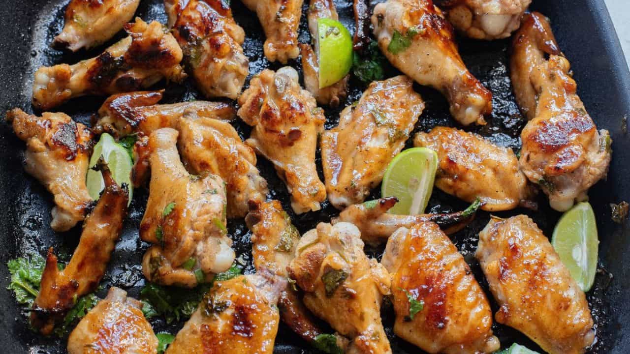 Grilled chicken wings arranged on a baking tray with fresh lime wedges and herb garnish.