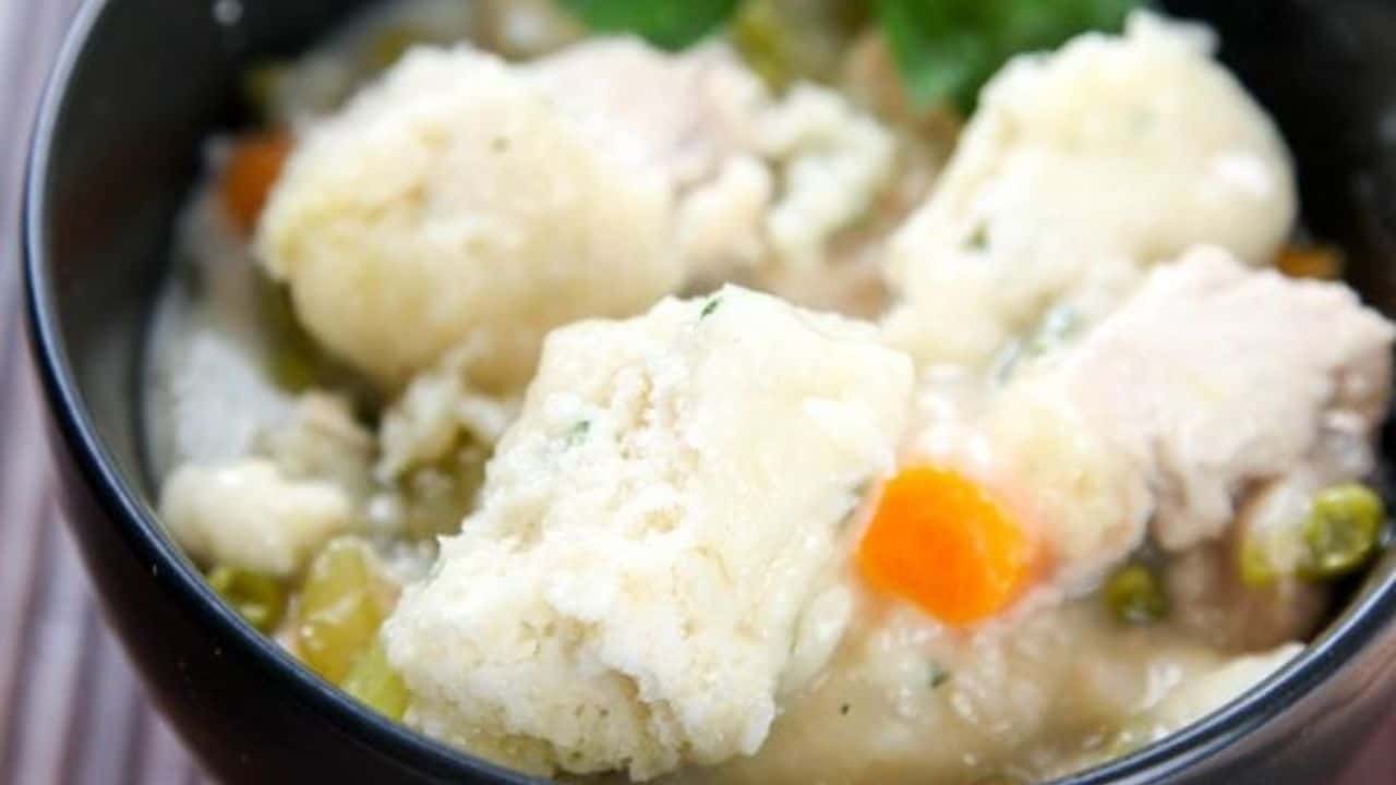 A bowl of chicken and dumplings with pieces of chicken, diced carrots, peas, and fluffy dumplings in a creamy broth.