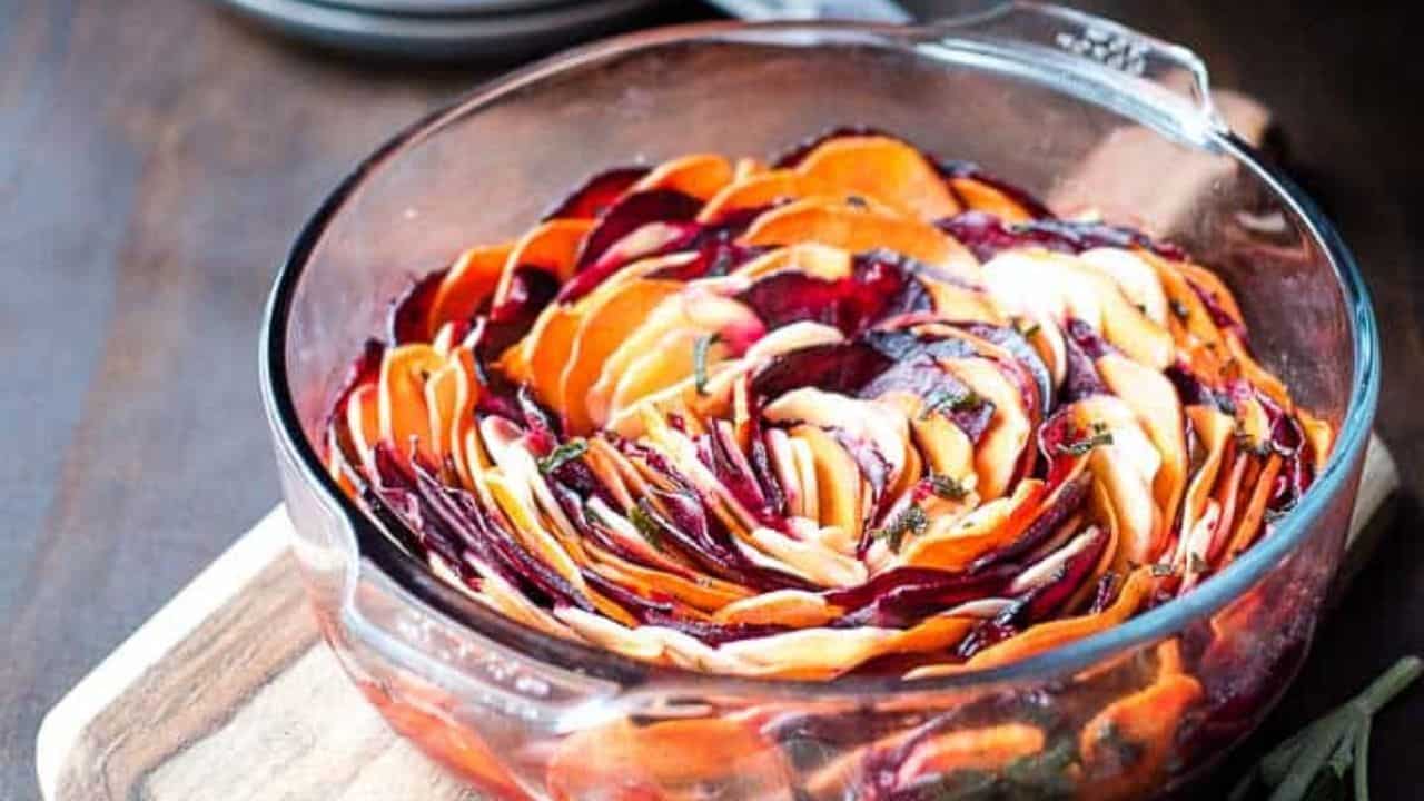 A dish of beets, sweet potatoes, and parsnips roasted in the oven with sprigs of sage.