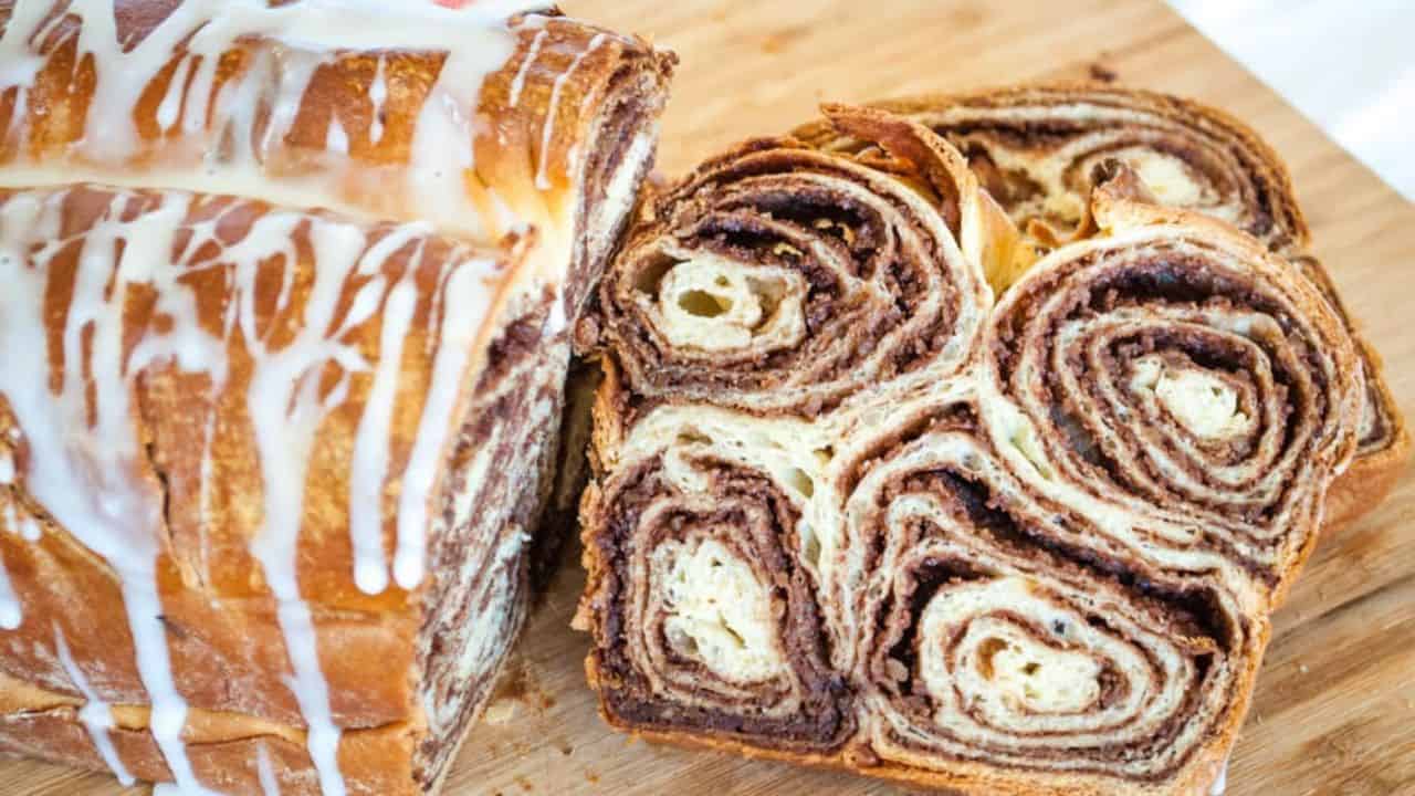 A sliced loaf of Povitica bread drizzled by icing in a wooden board.
