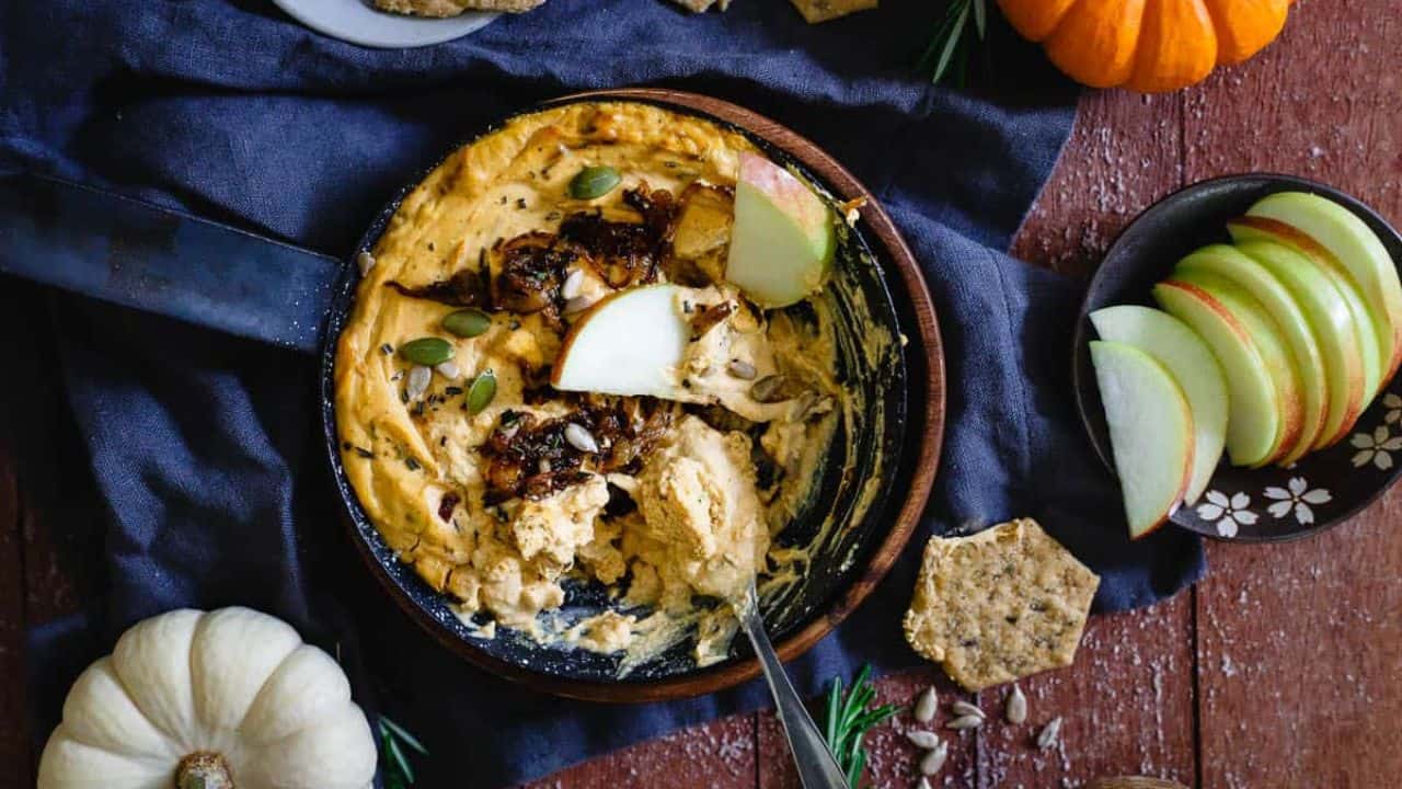 Pumpkin goat cheese dip topped with caramelized onions, sunflower seeds and pepitas in a small skillet.