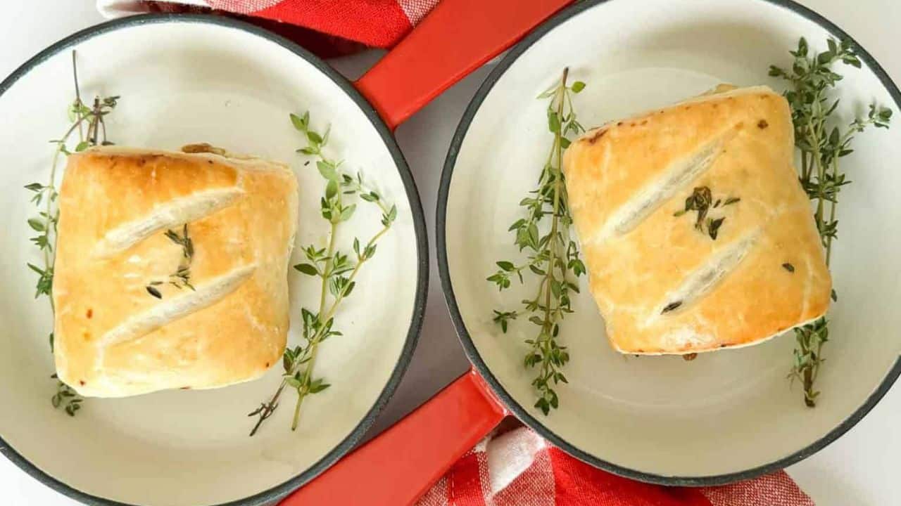 Two sausage rolls with thyme on a red and white checkered tablecloth, perfect for winter dinners.