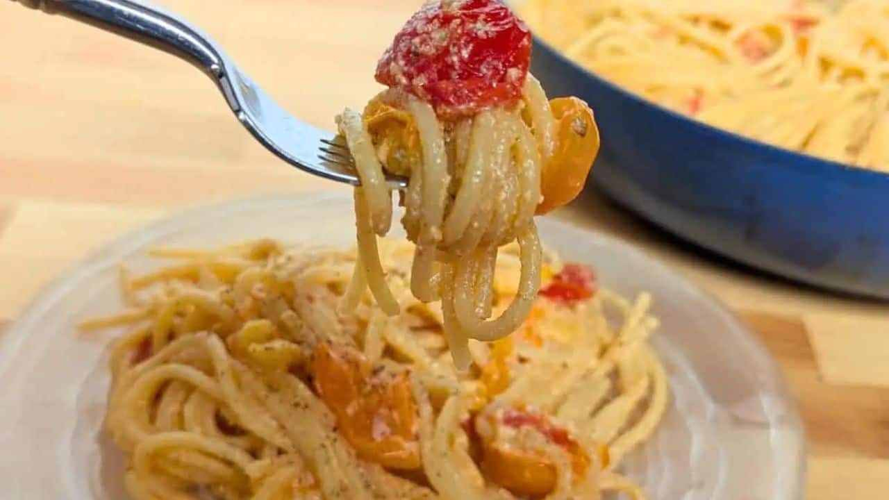 Image shows a clear glass plate of spaghetti with yellow and red tomatoes, lightly coated in sauce and sprinkled with black pepper, on a wooden surface.