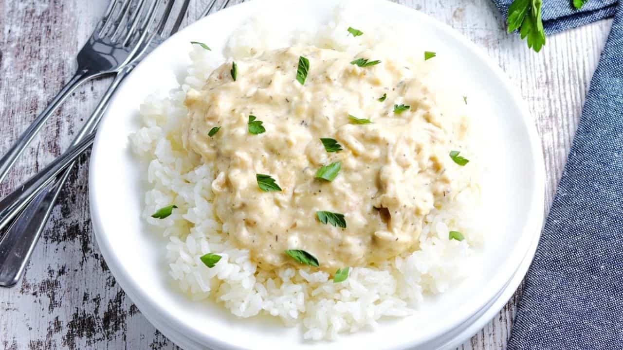 Slow Cooker Creamy Chicken on a white plate on rice topped with parsley.