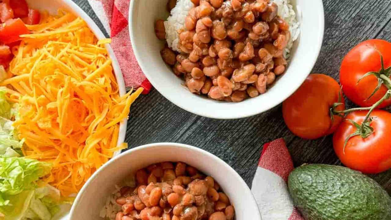 A slow cooker filled with simmering pinto beans in a thick, tomato-based sauce with a visible spoon.