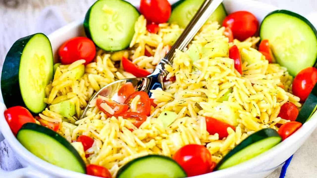 Summer orzo pasta salad in a while serving bowl on a whitewashed background next to a bowl of green beans.