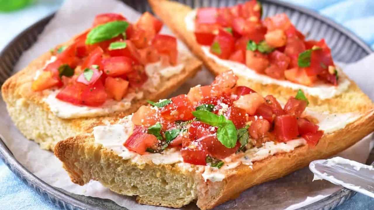 Three slices of toasted bread topped with a tomato mixture, herbs, and grated cheese are arranged on a round plate lined with parchment paper.
