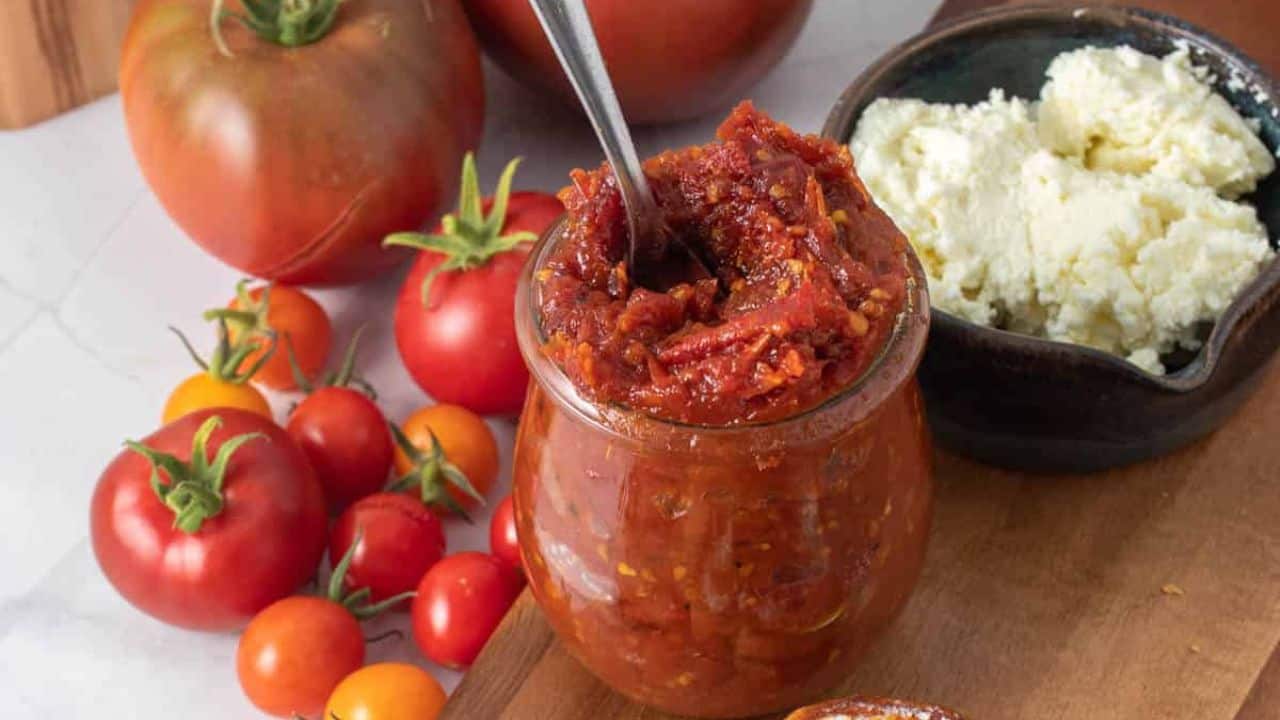 A close up image of a glass jar filled with tomato miso jam sits on a wooden board.