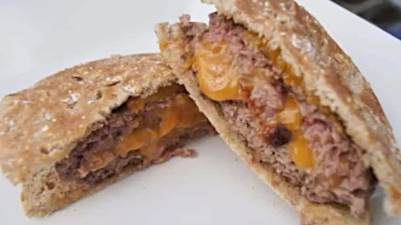 Bacon cheddar stuffed burger cut in half and on a white plate.