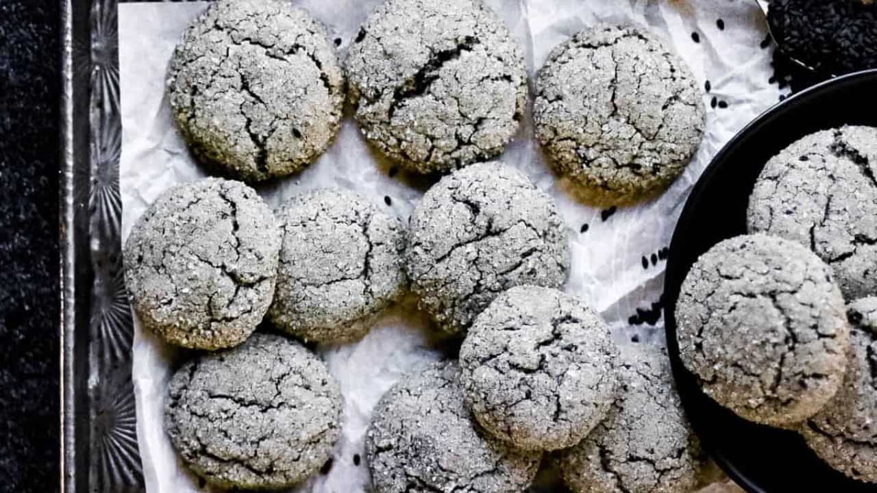 Black sesame cookies on a baking sheet with a spoonful of black sesame seeds.