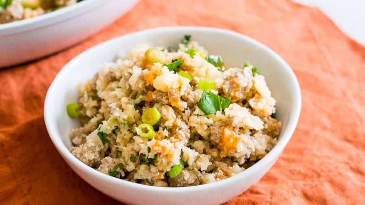 White skillet with buffalo ground turkey and cauliflower rice with a wooden spoon.