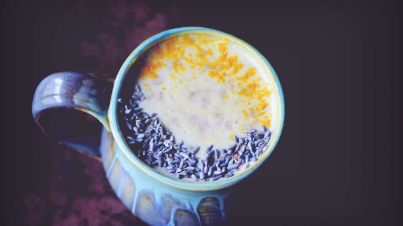 A ceramic mug filled with a yellow frothy beverage, topped with dried lavender flowers on one side.