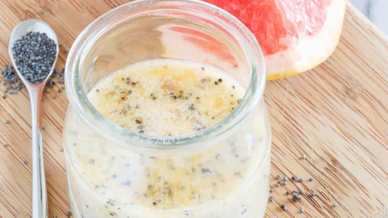 A glass of grapefruit dressing with poppyseeds seeds and a spoon.