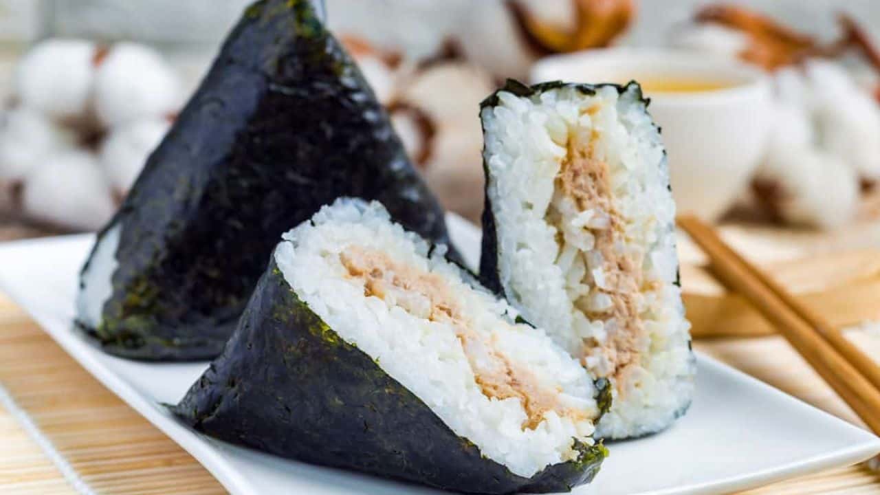 Two pieces of onigiri on a plate with chopsticks.