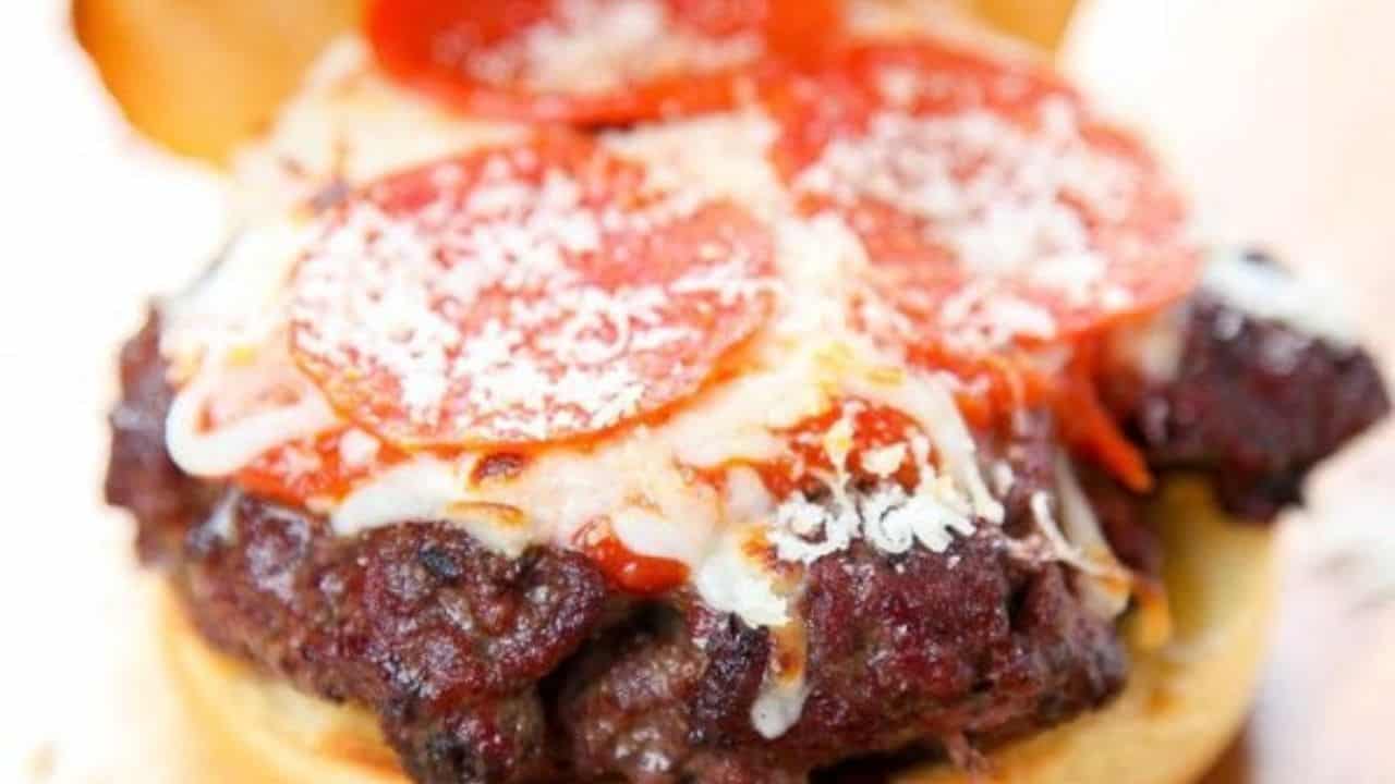 A hamburger patty topped with melted cheese, tomato sauce, sliced pepperoni, and grated cheese on a bun.