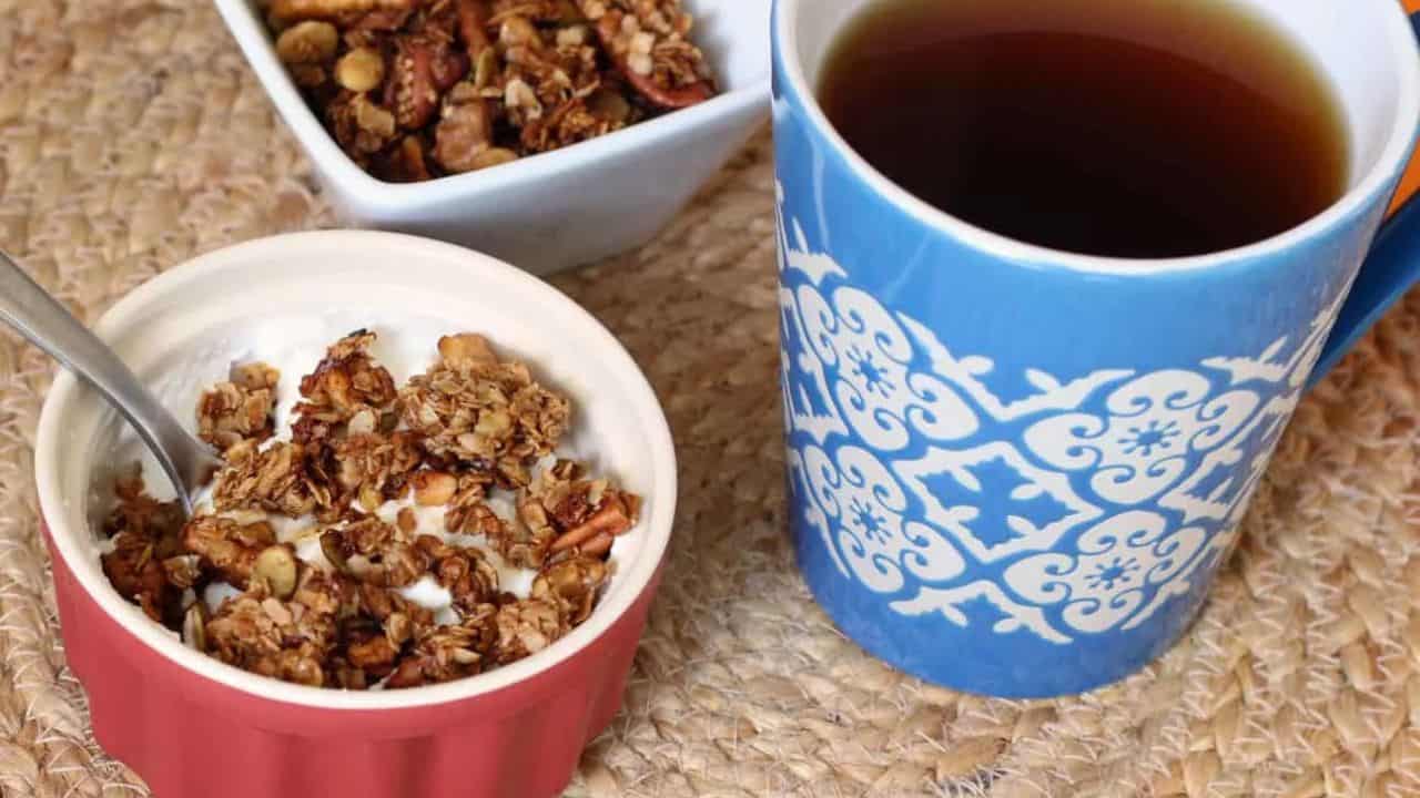 Bowl of yogurt topped with granola next to a cup of coffee.