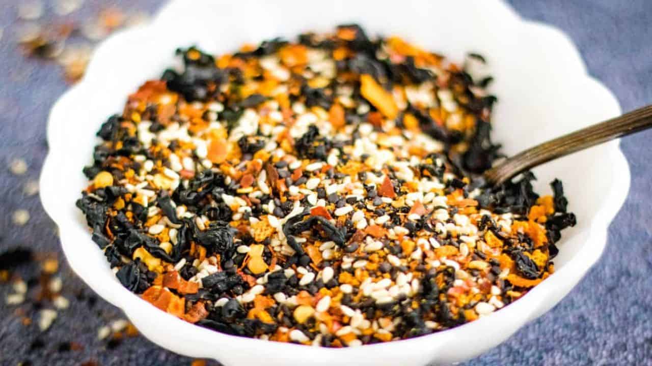 Low angle shot of a white bowl filled with shichimi togarashi with a spoon in it.