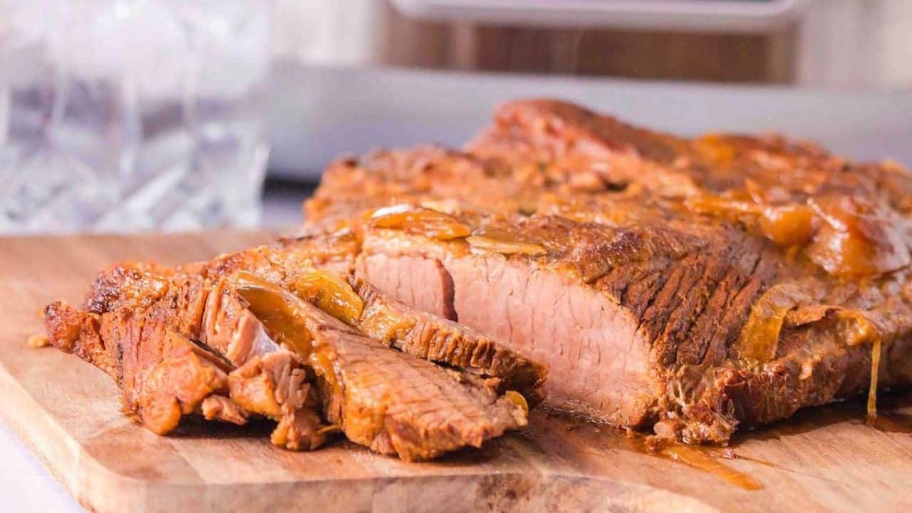 Cooked beef brisket sliced on a wooden cutting board, showing a tender and juicy interior.