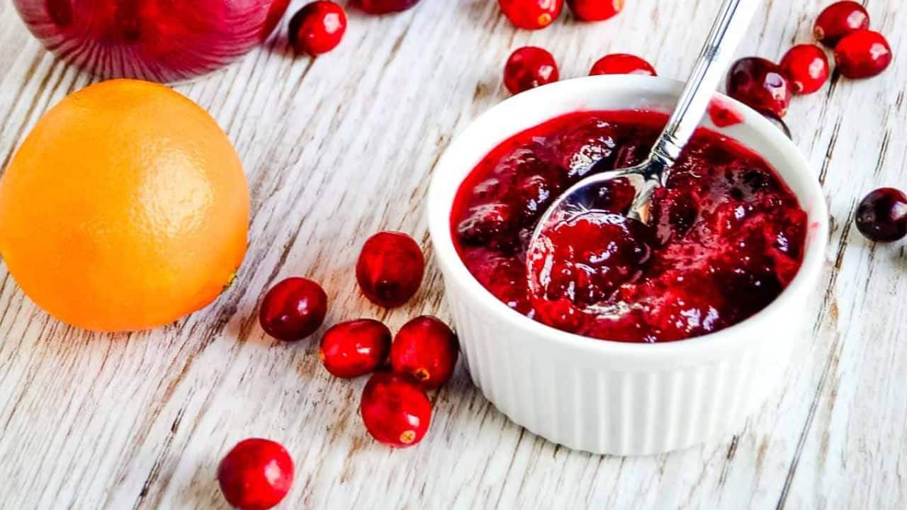 Small jar of clementine cranberry jam with fresh fruit nearby.