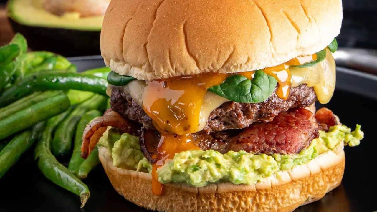 An up-close shot of bacon-avocado ground beef burger on a flat white surface.