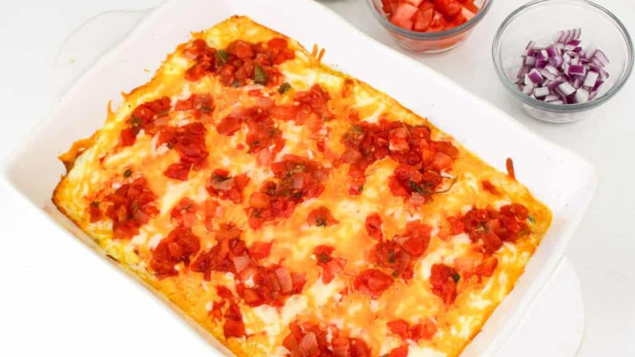 Casserole dish with melted cheese, diced tomatoes, onions, and chopped cilantro on top, with a side bowl of salsa and cilantro garnish nearby.