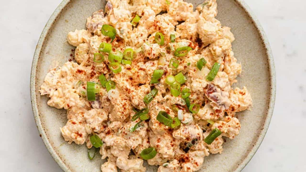 Cauliflower potato salad garnished with green onions in a bowl with a fork.