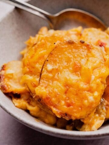 A bowl of cheesy scalloped potatoes with a serving spoon resting inside.