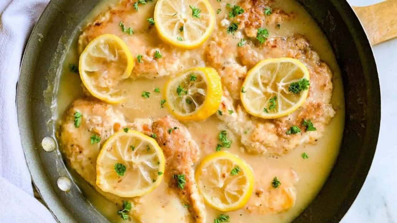 A skillet filled with lemon chicken in sauce with lemon slices.