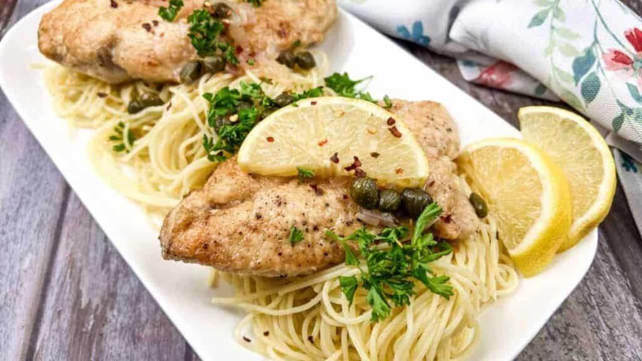 Two chicken piccata on a white plate with parsley and lemon wedges.