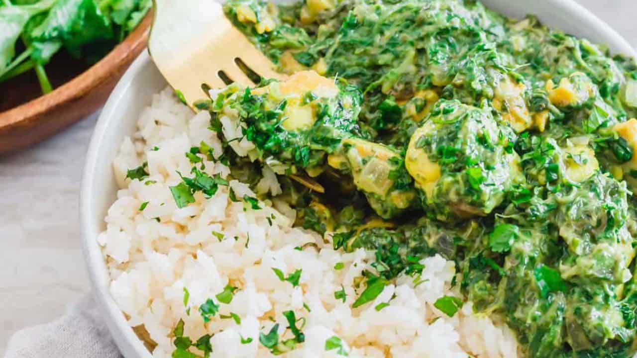 A bowl of white rice garnished with chopped herbs next to a creamy spinach and cheese curry, with a fork resting on the food.