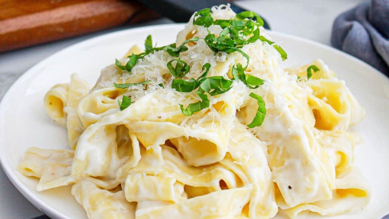 A bowl of creamy pasta topped with grated cheese and parsley, set on a textured placemat.