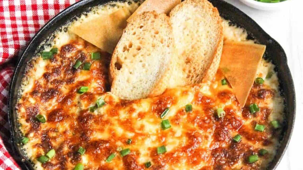 A person dipping a piece of bread into a skillet of cheesy dip.
