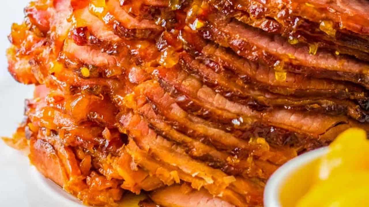 Spiral ham on a plate with asparagus and peaches in the background.