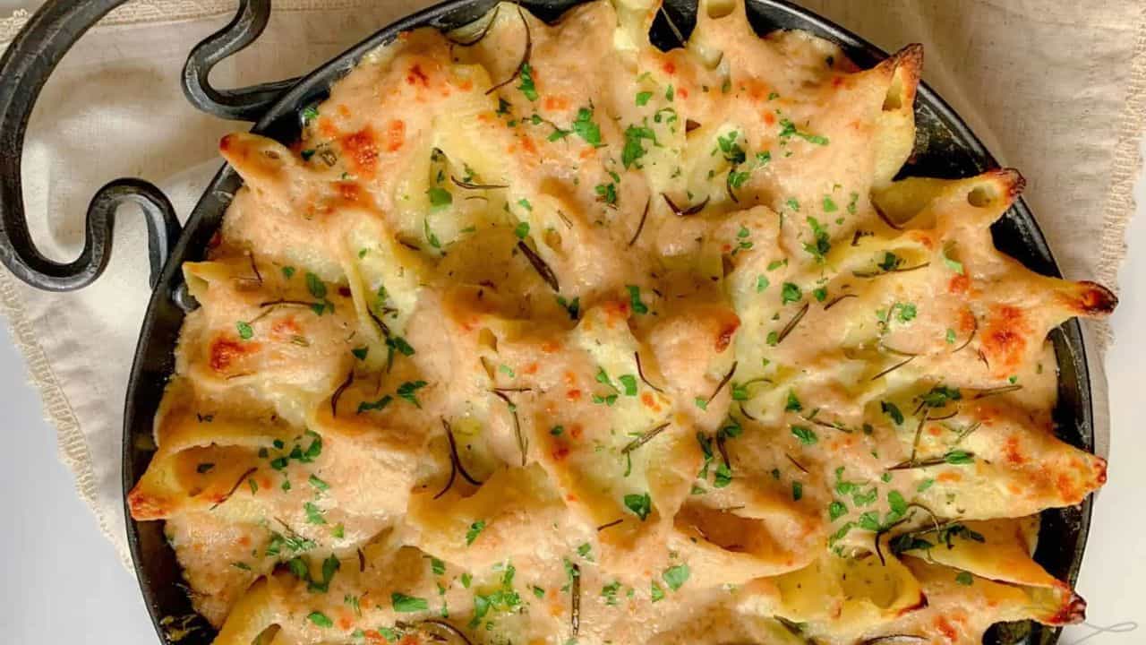 A cast iron pan filled with stuffed shells covered in cheese and a white sauce.