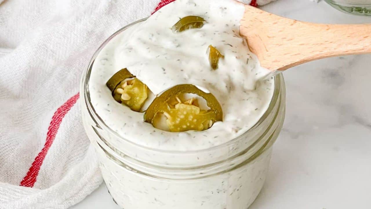 A jar of jalapeño ranch salad dressing with slices of jalapeño on top.
