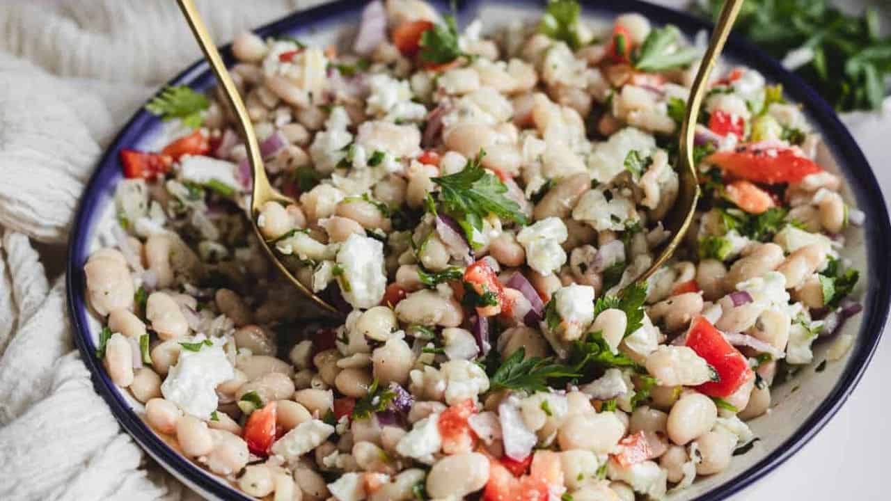 Side view of white bean salad in bowl with tongs.